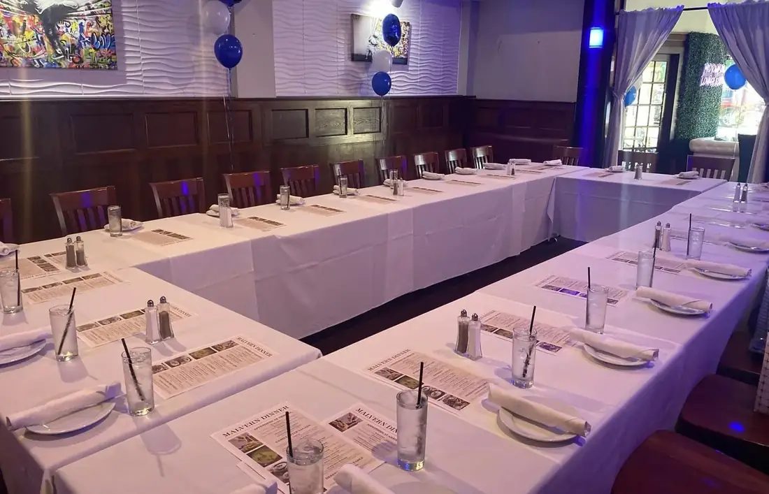 Long banquet tables in white linen set for a school dinner with printed menus and balloons.