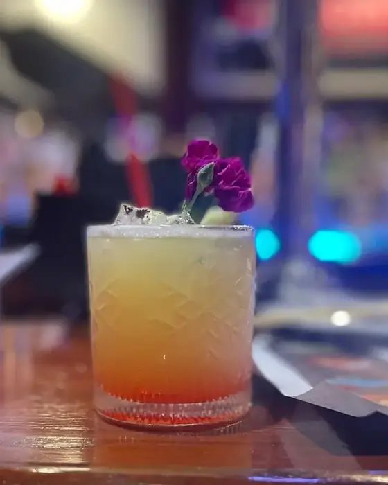 An amber layered cocktail garnished with a purple flower on the bar at 660 LIVE.