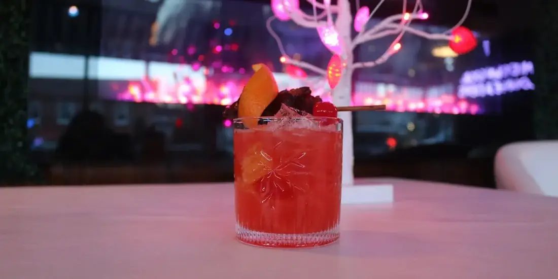 A red signature cocktail with orange, cherry and cinnamon garnish on the bar at 660 LIVE.