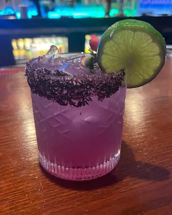 A violet cocktail with a hibiscus salt rim and lime wheel on the bar at 660 LIVE.