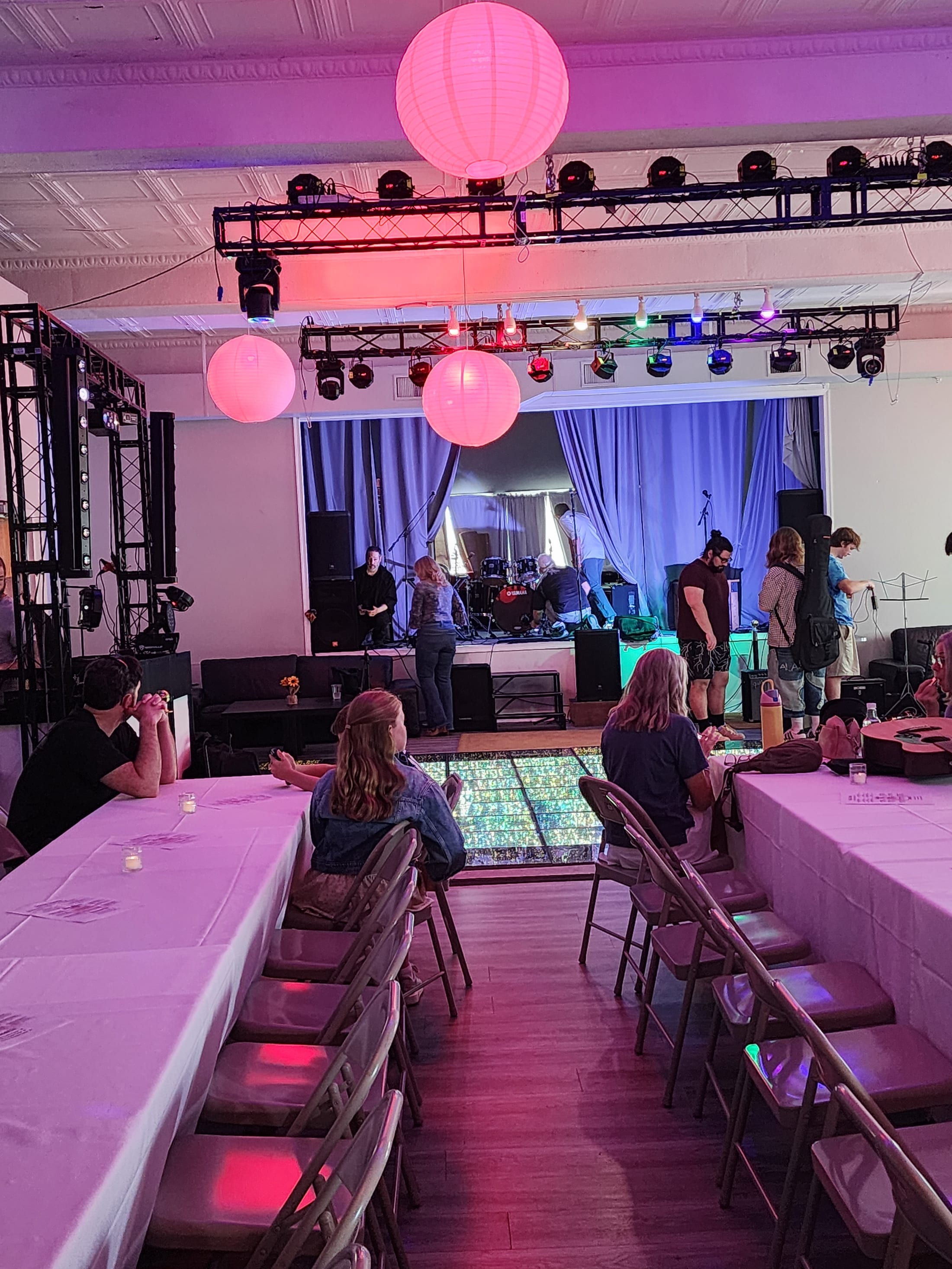 A band playing the stage in The Loft at 660, pink paper lanterns overhead, coloured stage lighting and guests at linen-covered tables