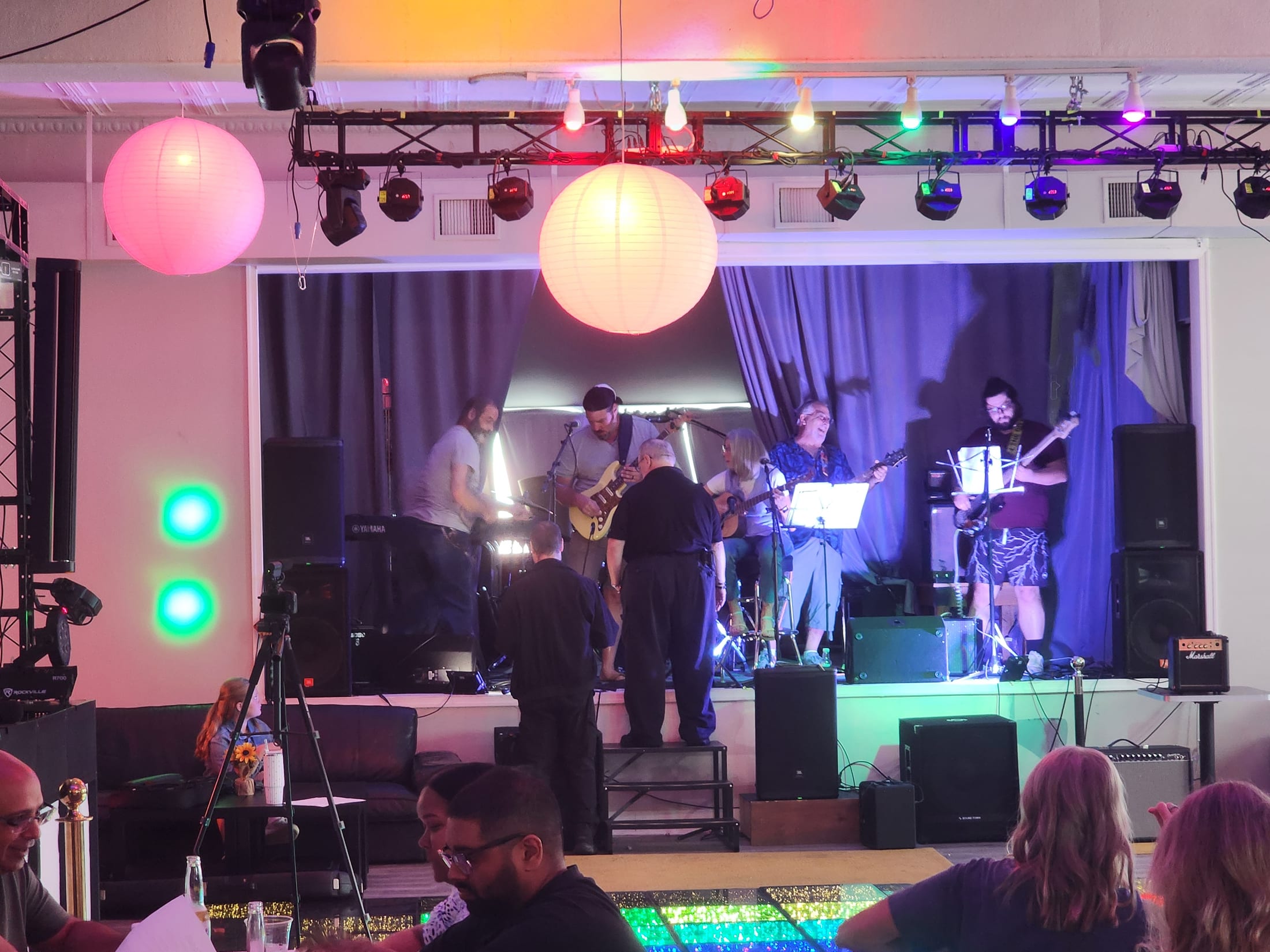 A full band mid-set on the stage at 660 LIVE, stage lighting rig lit, audience watching from the floor