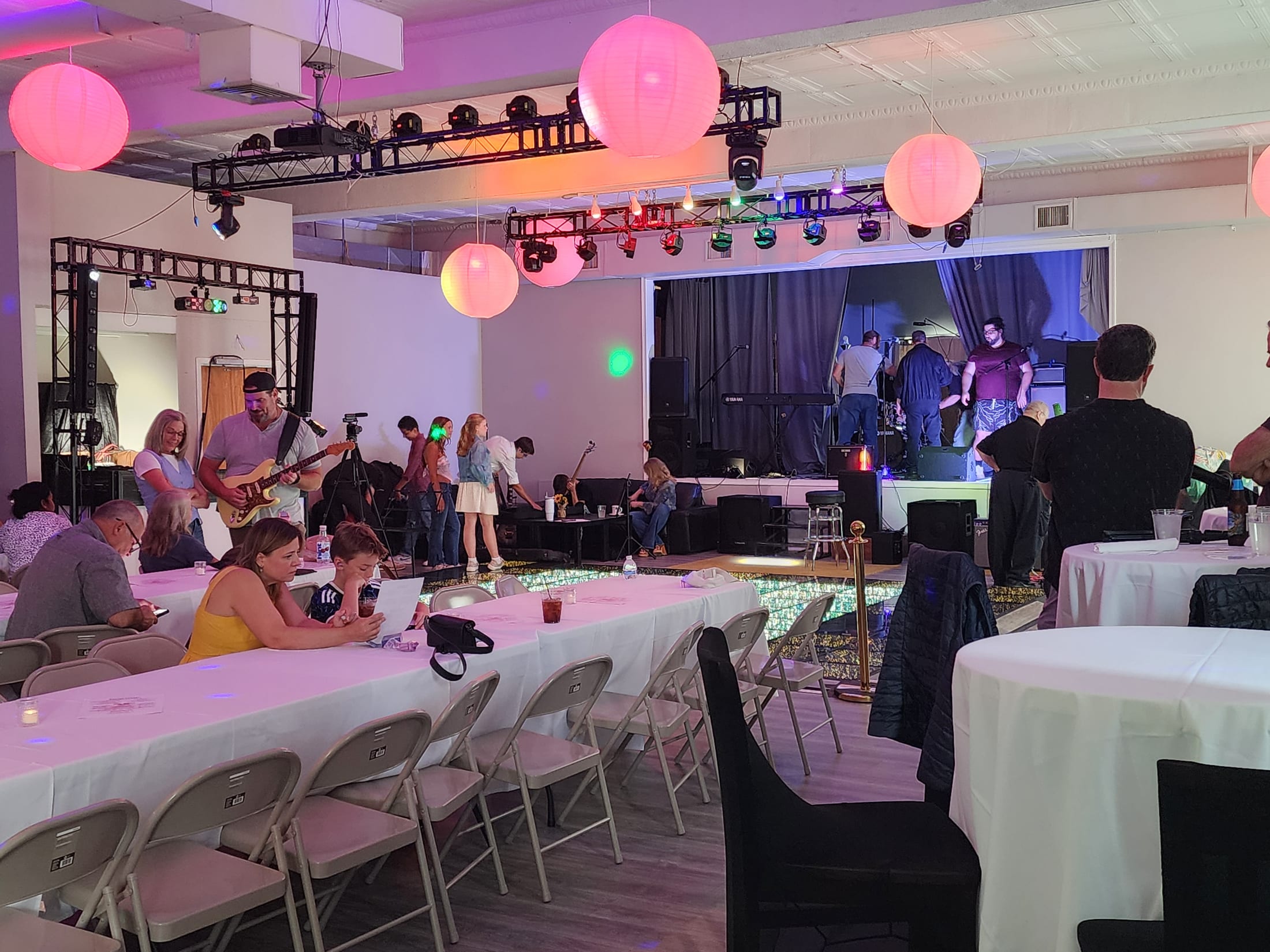 A wide view of The Loft during a live music night, guests standing and seated, lanterns and coloured lighting overhead
