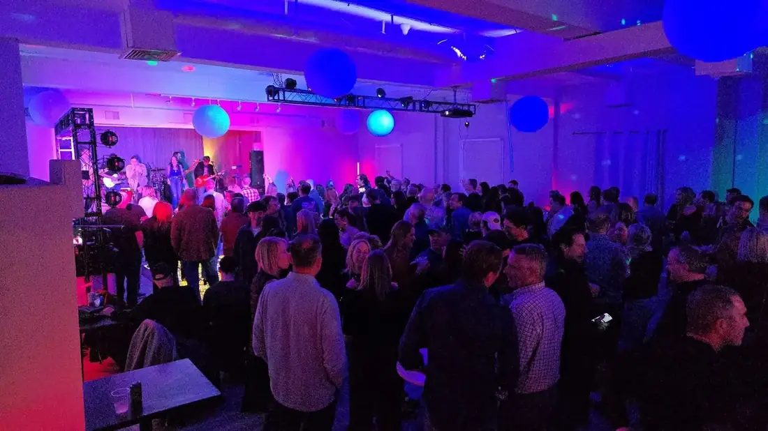 The Loft at 660 packed with several hundred guests watching a live band on stage, the room lit blue and purple.