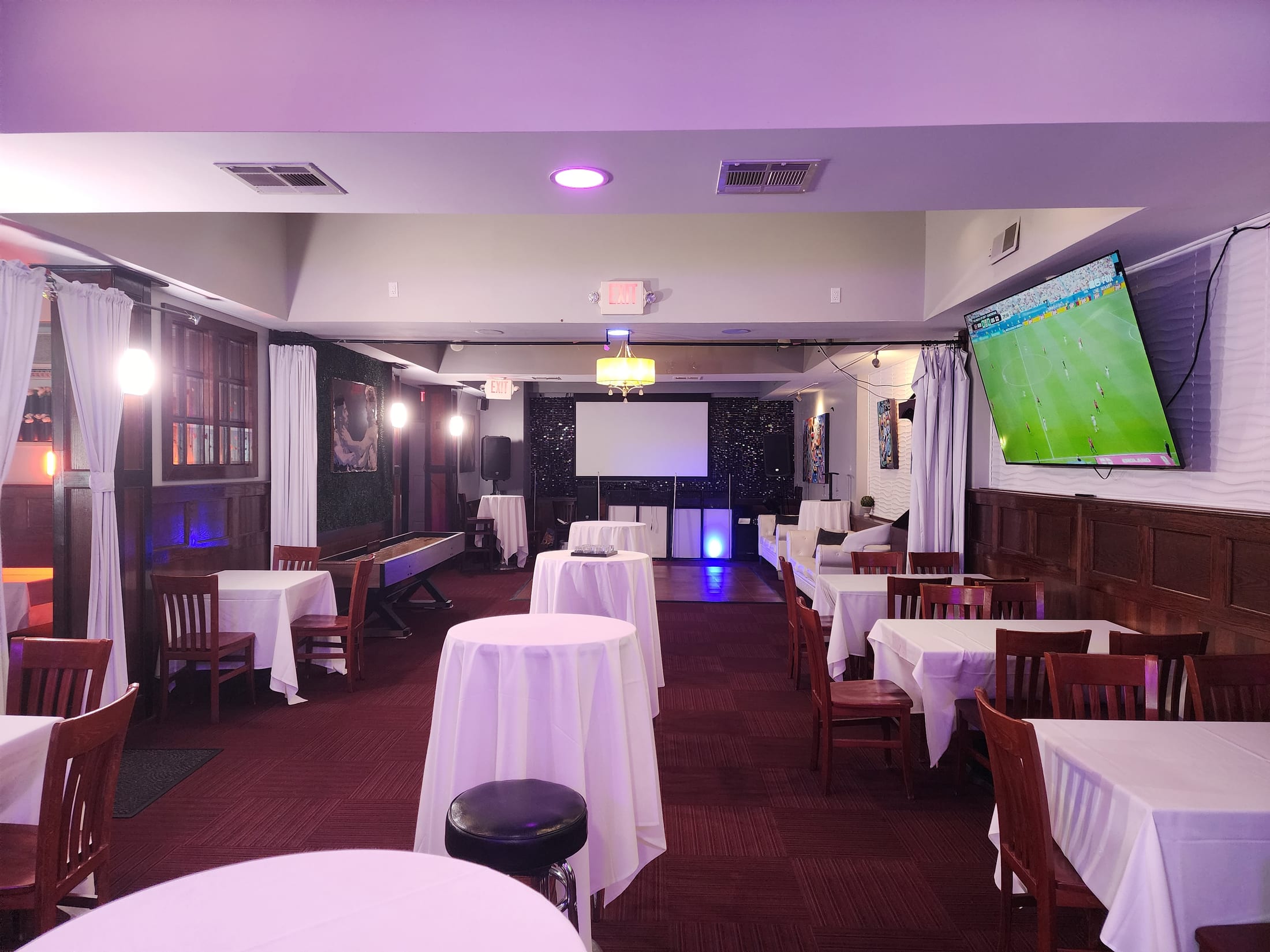 The Loft set for a seated dinner with draped tables and chairs, purple lighting and a projection screen at the far end