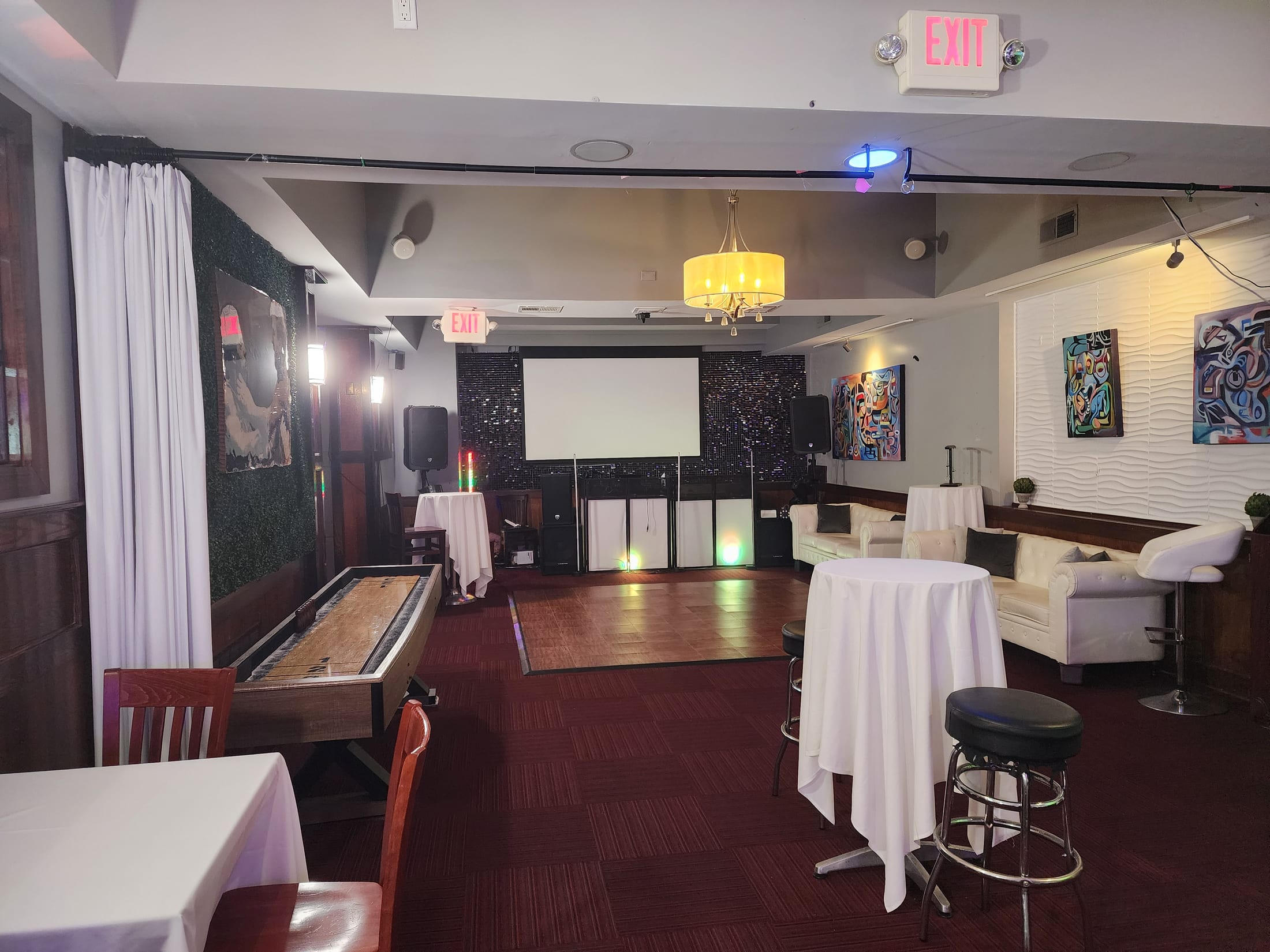 The Loft at 660 set for a private event — white linen cocktail tables, lounge seating, shuffleboard table, projection screen and chandelier