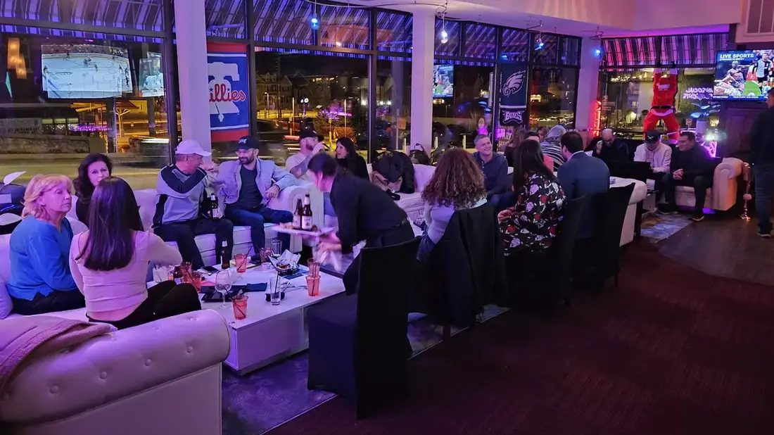 The first-floor lounge at 660 LIVE on a busy night — white sofas full of guests, sport on the big screens and Lancaster Avenue through the windows.