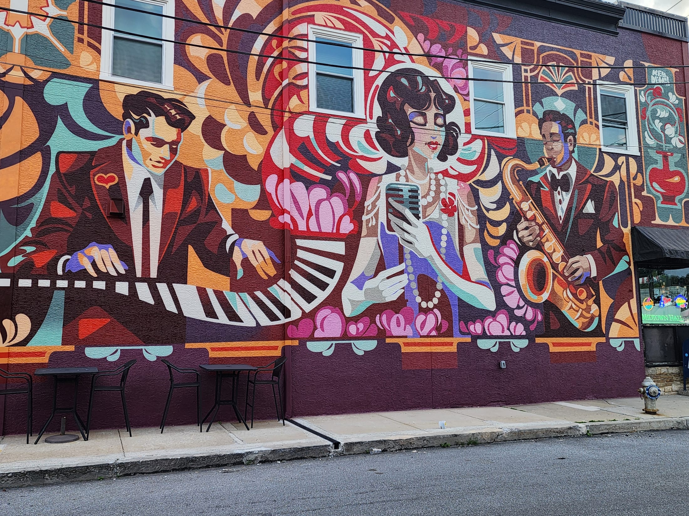 The mural on the side of 660 LIVE in Berwyn — an art deco jazz band with a pianist, a singer at a ribbon microphone and a saxophone player, with bistro tables set out along the pavement below